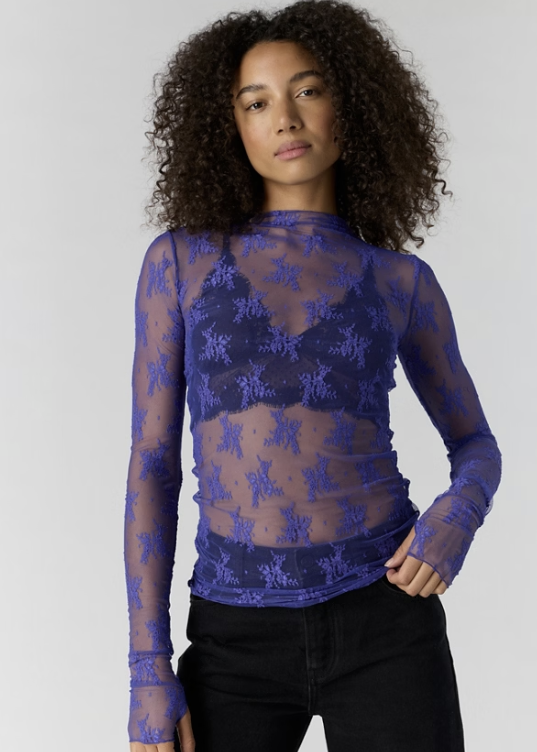 Woman wearing blue lace top over bralette and black pants on white background