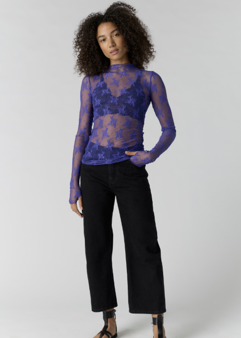 Woman wearing blue lace top over bralette and black pants on plain background