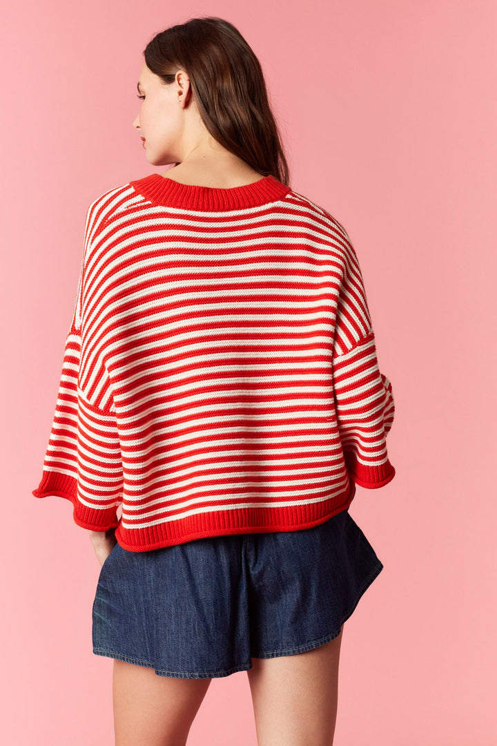 Back of woman wearing red and white stripe short sleeve cardigan and denim mini skirt on plain background