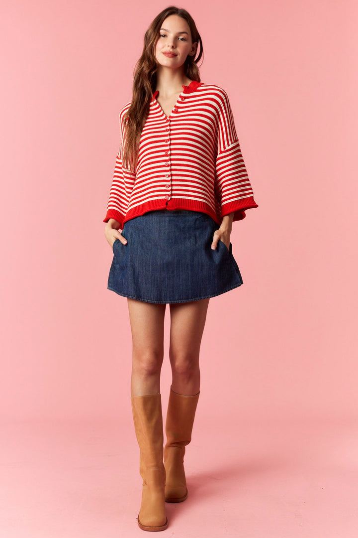Woman wearing red and white stripe short sleeve cardigan and denim mini skirt on plain background