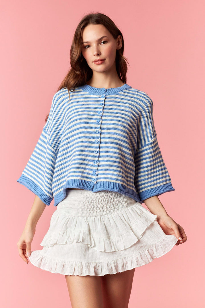 Woman wearing blue and white stripe short sleeve cardigan and white mini skirt on plain background