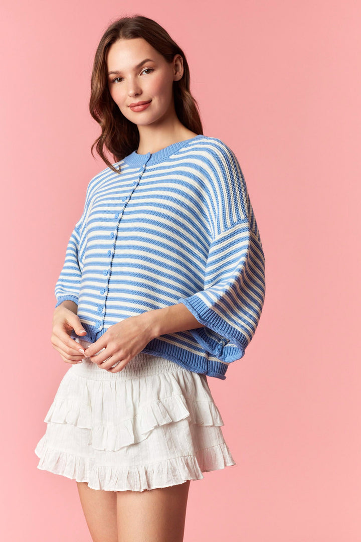 Woman wearing blue and white stripe short sleeve cardigan and white mini skirt on plain background