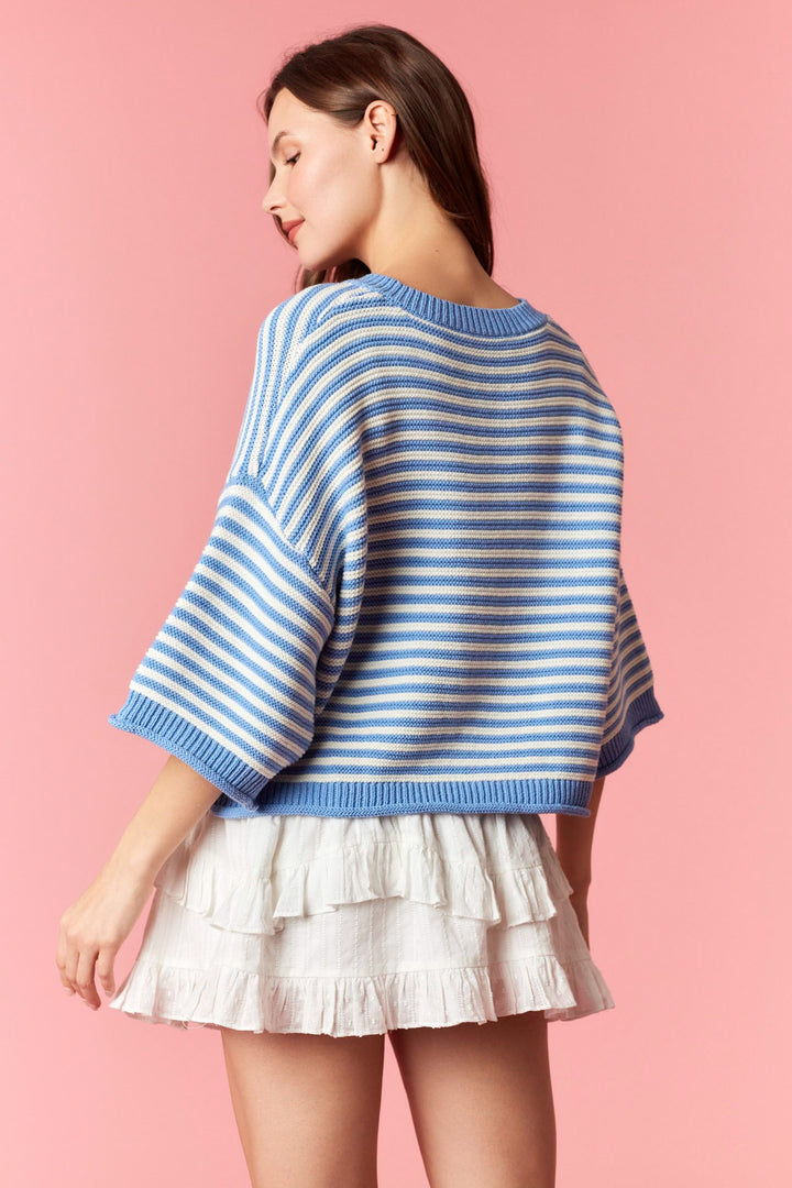 Back of woman wearing blue and white stripe short sleeve cardigan and white mini skirt on plain background