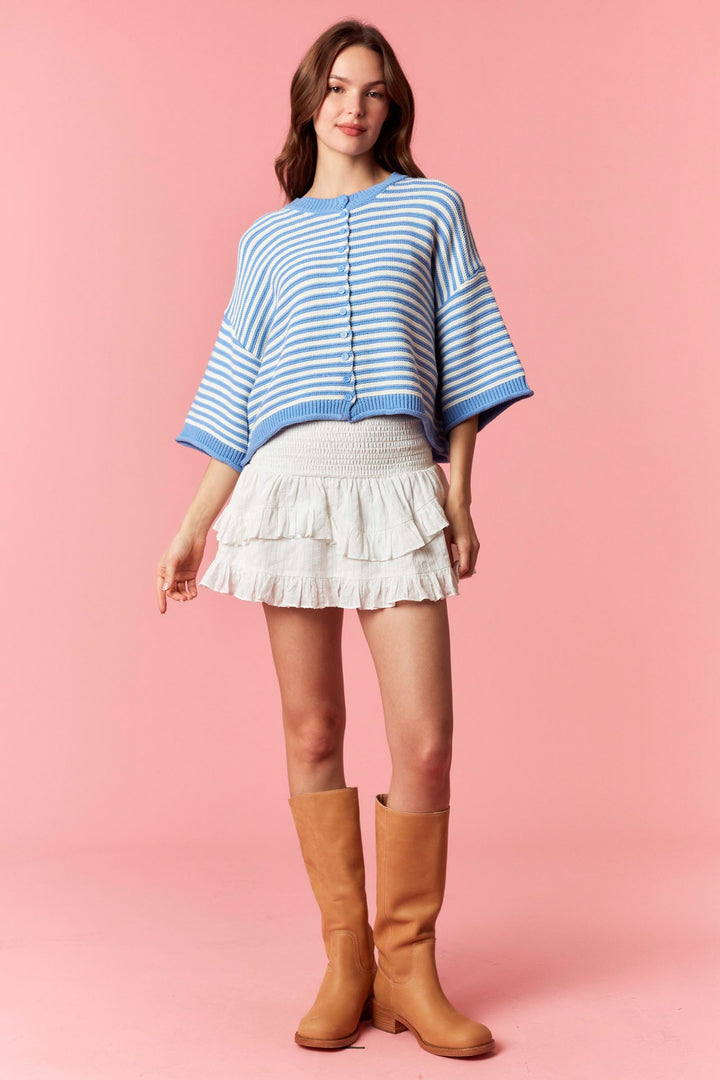 Woman wearing blue and white stripe short sleeve cardigan and white mini skirt on plain background