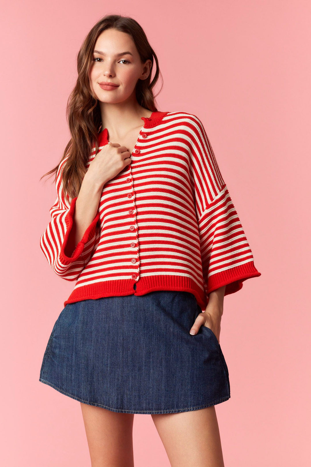 Woman wearing red and white stripe short sleeve cardigan with denim mini skirt on plain background