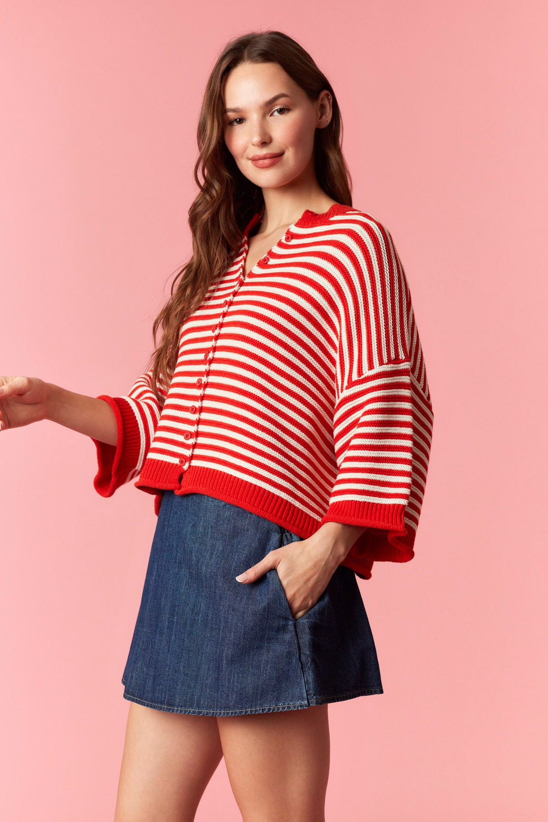 Woman wearing red and white stripe short sleeve cardigan and denim mini skirt on plain background