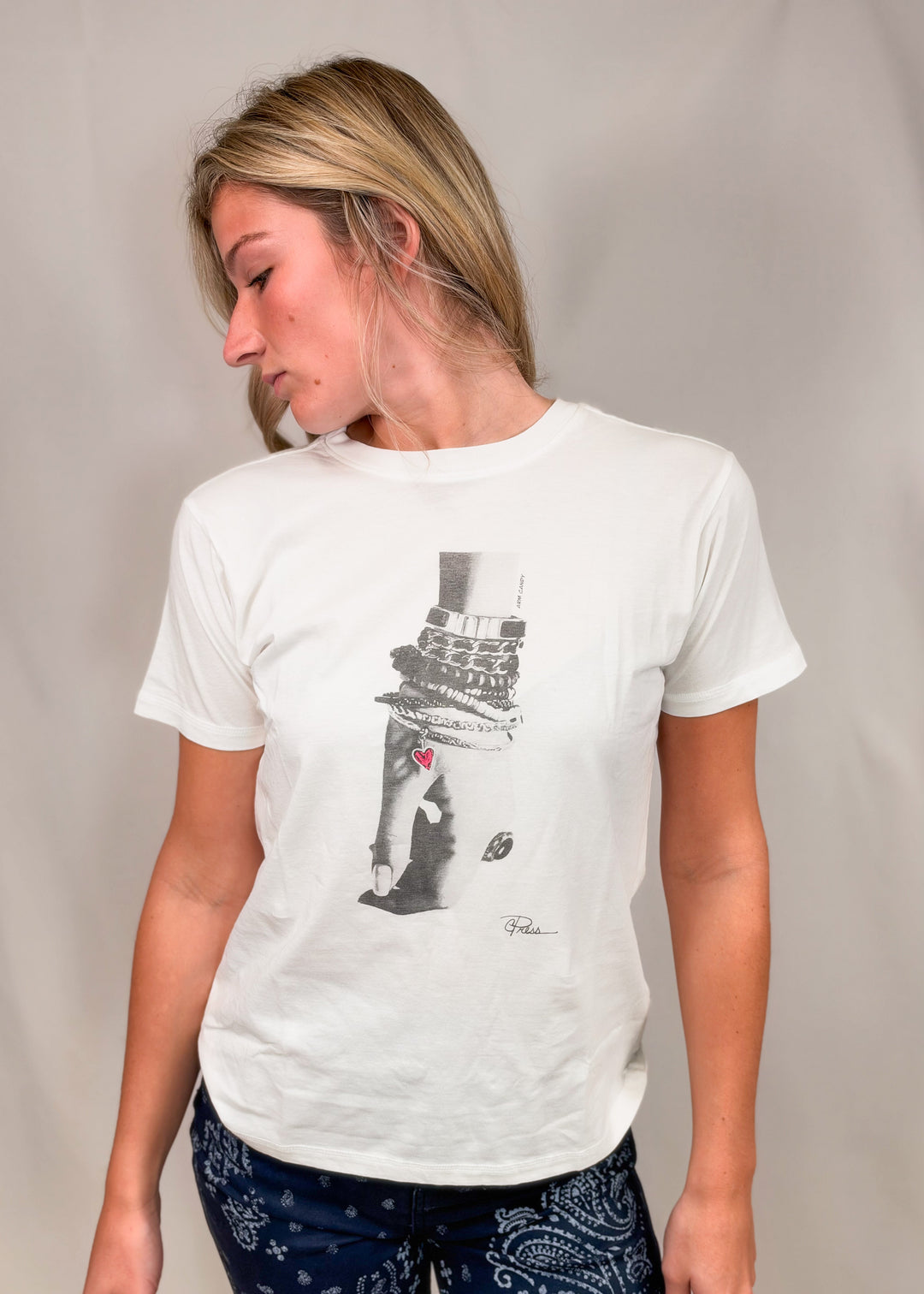 Woman wearing graphic tee with drawn hand and bracelets with heart on plain background