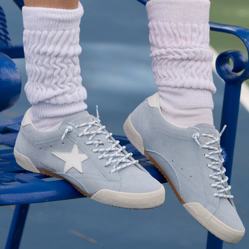 Gray sneakers with a star design worn with white socks on a blue chair.
