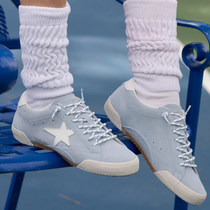 Gray sneakers with a star design worn with white socks on a blue chair.