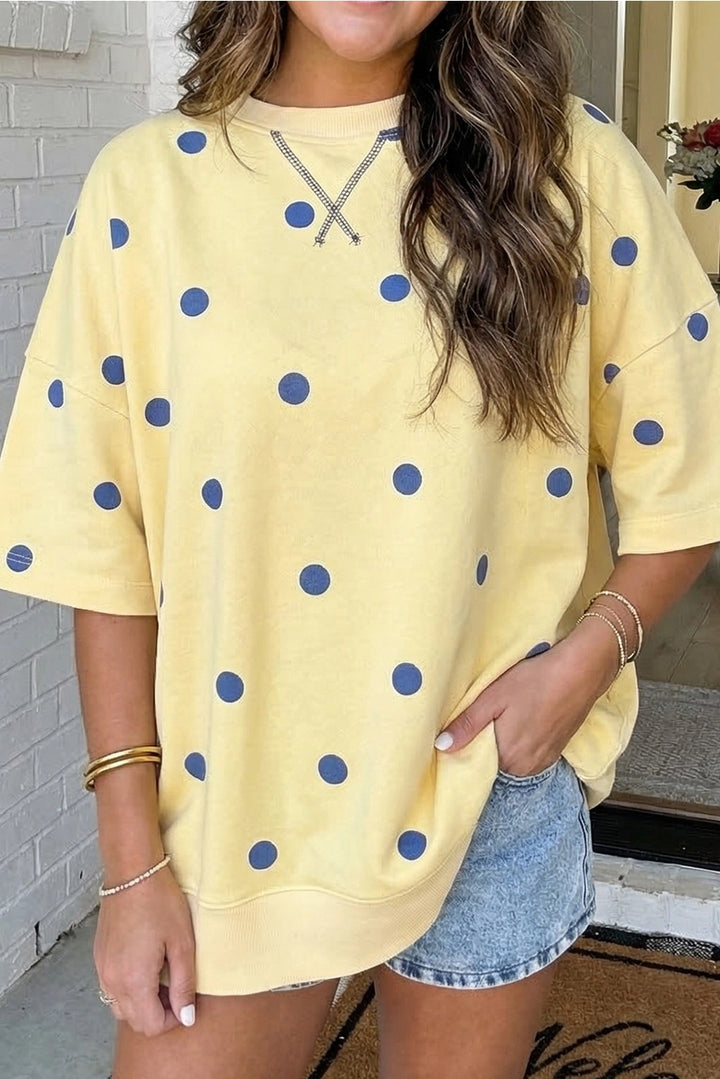 Person wearing a yellow sweatshirt with blue polka dots and denim shorts.