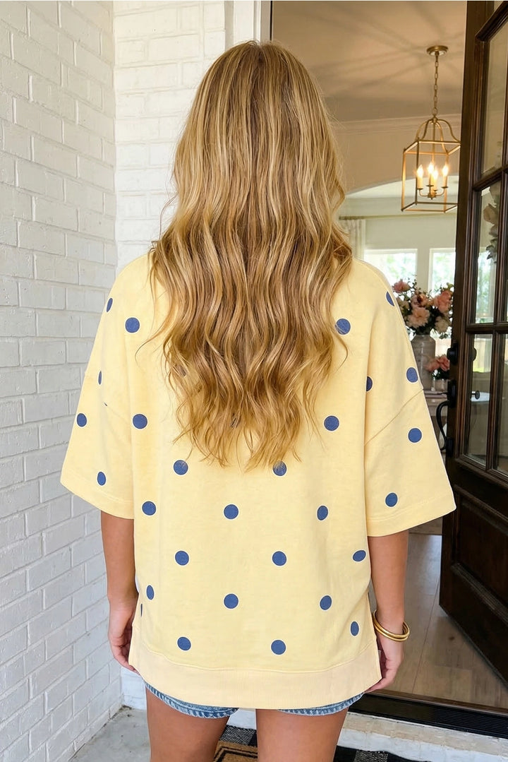 Person wearing a yellow polka dot shirt standing in a room with a mirror and light fixture.