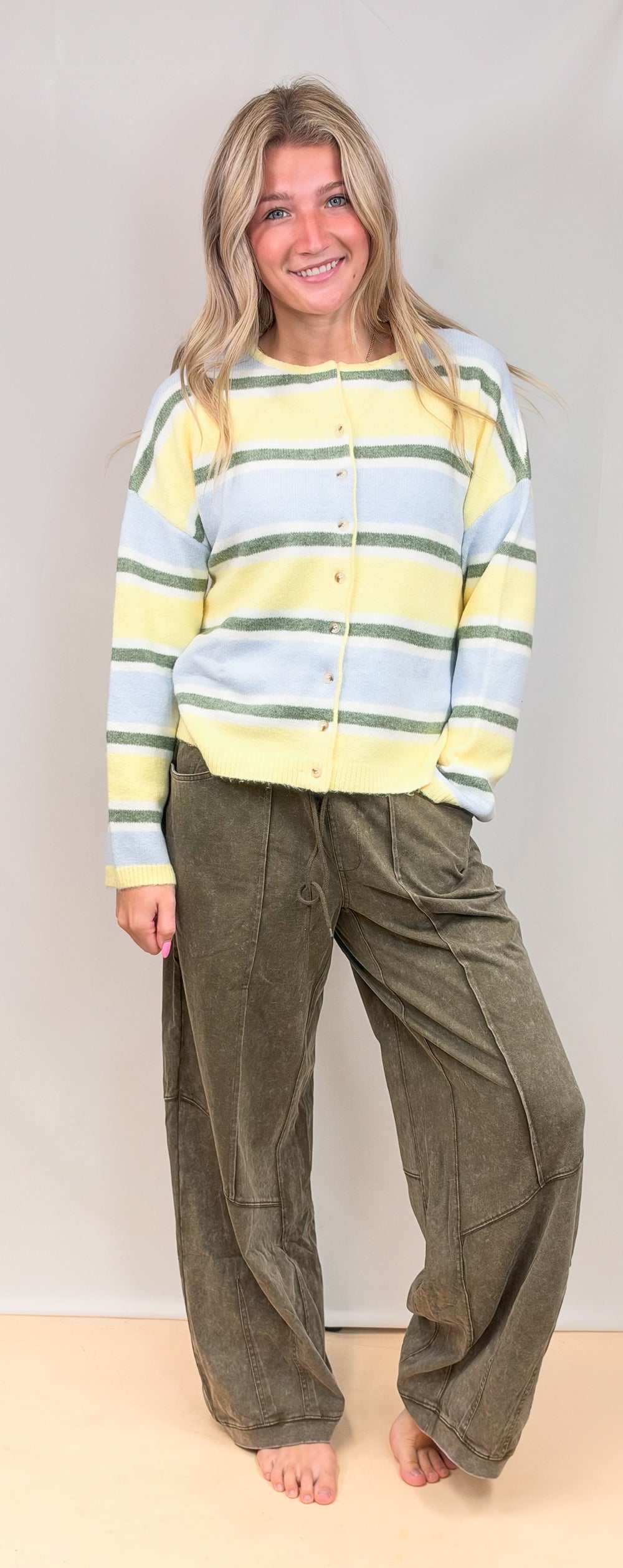 Woman wearing yellow, blue and green stripe cardigan with green pants on plain background
