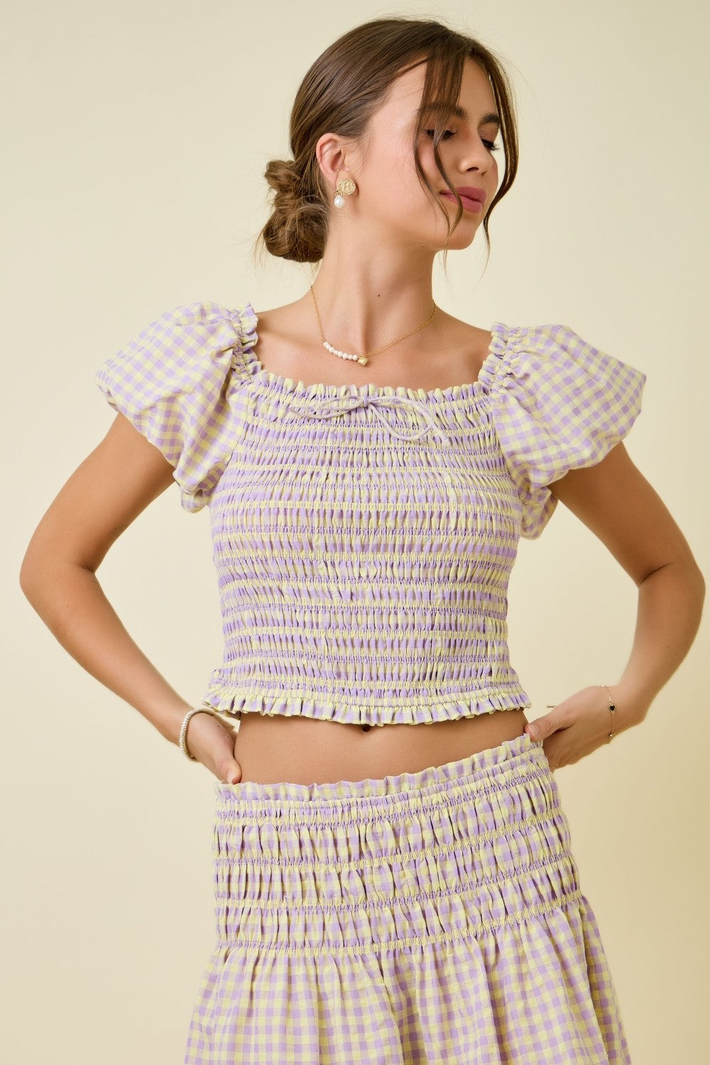 Woman wearing a checkered outfit with ruffled sleeves against a beige background