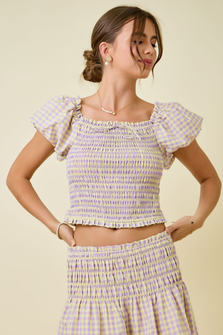 Woman wearing a checkered outfit with ruffled sleeves against a beige background