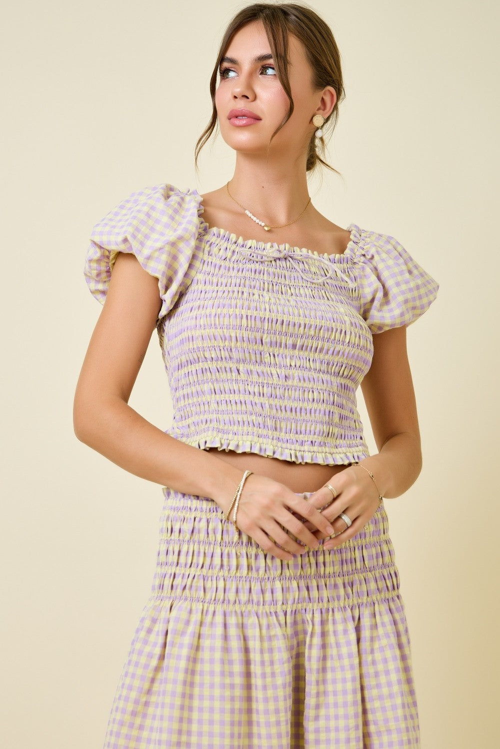 Woman wearing a checkered dress with ruffled sleeves against a beige background