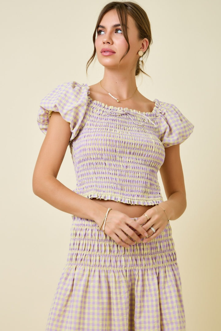 Woman wearing a checkered dress with ruffled sleeves against a beige background