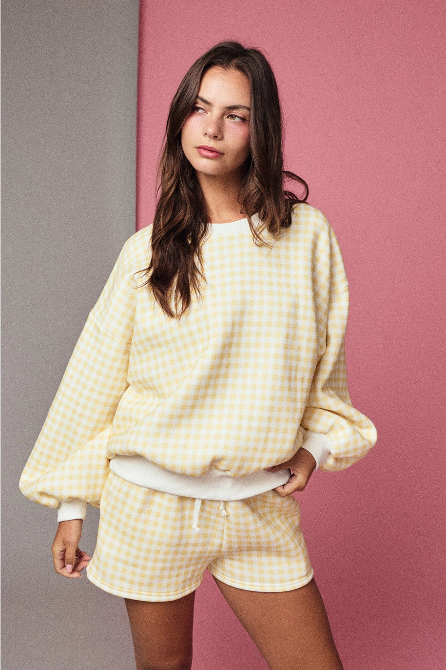Woman wearing matching yellow gingham set on pink background