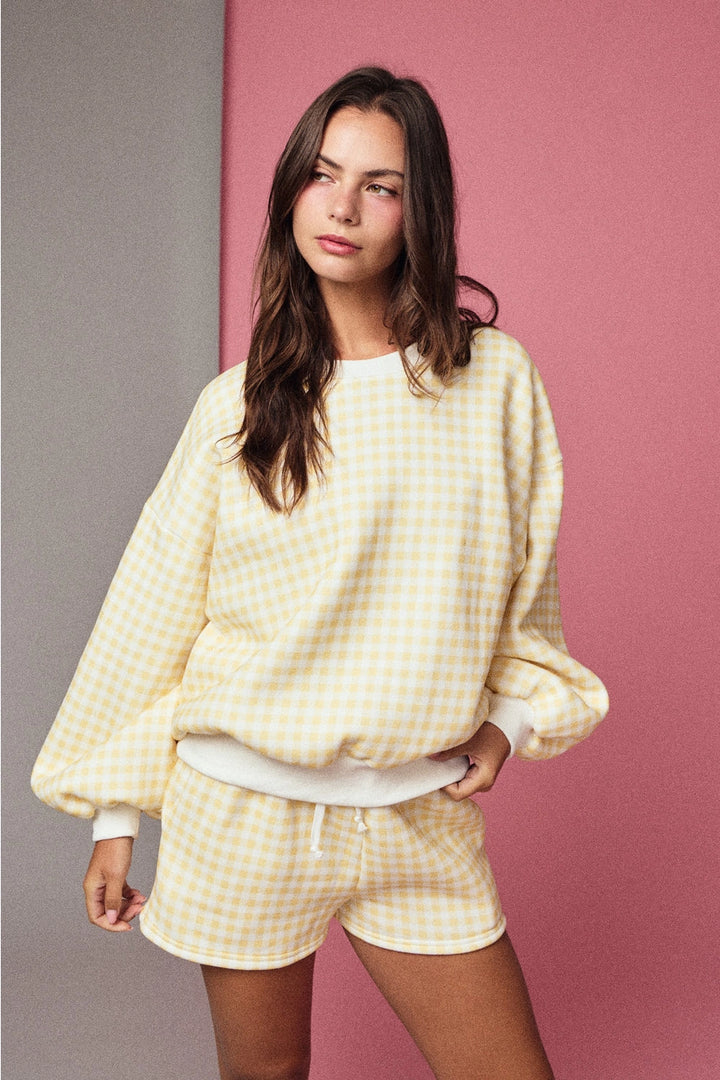 Woman wearing matching yellow gingham set on pink background