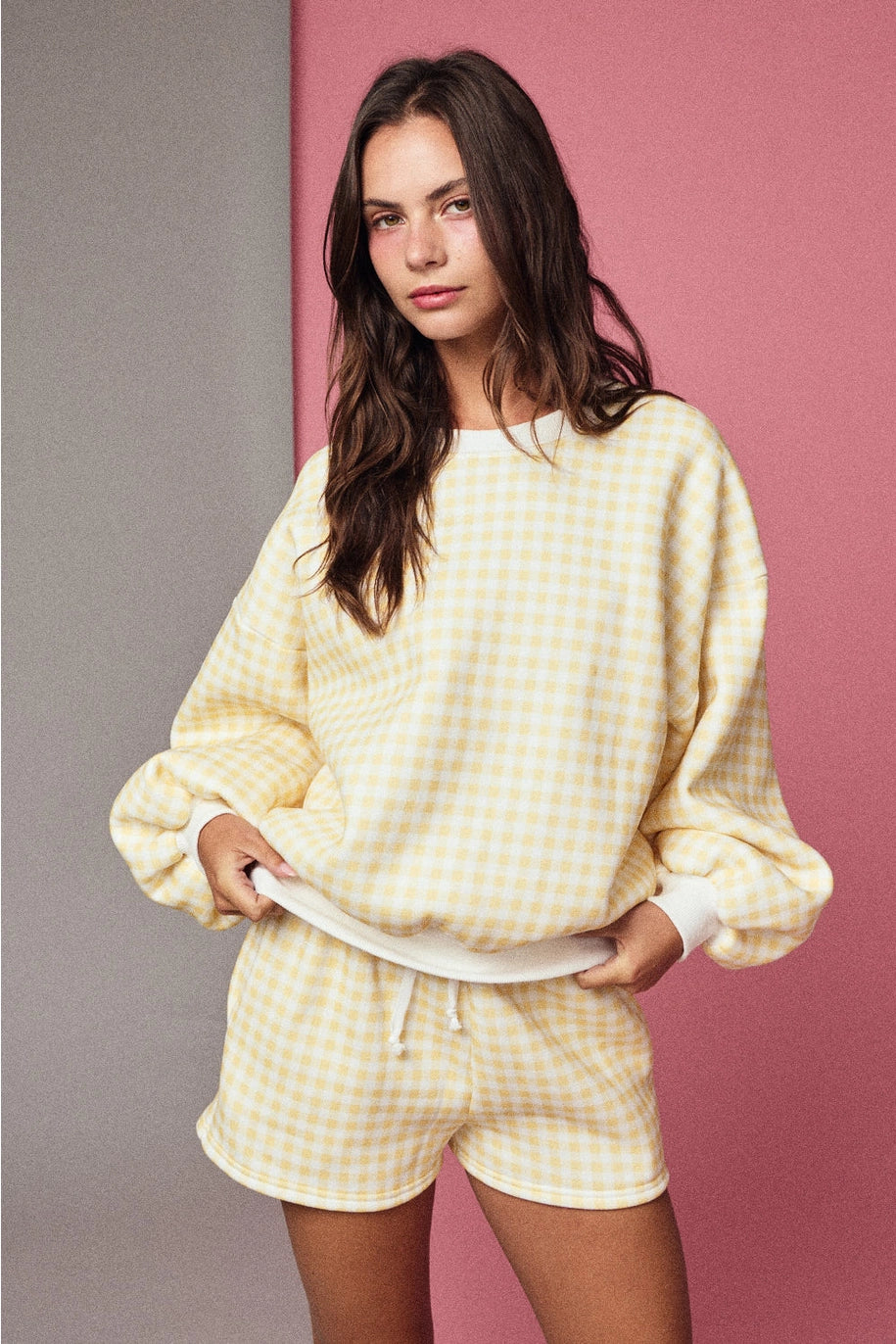 Woman wearing a yellow checkered outfit against a pink and gray background