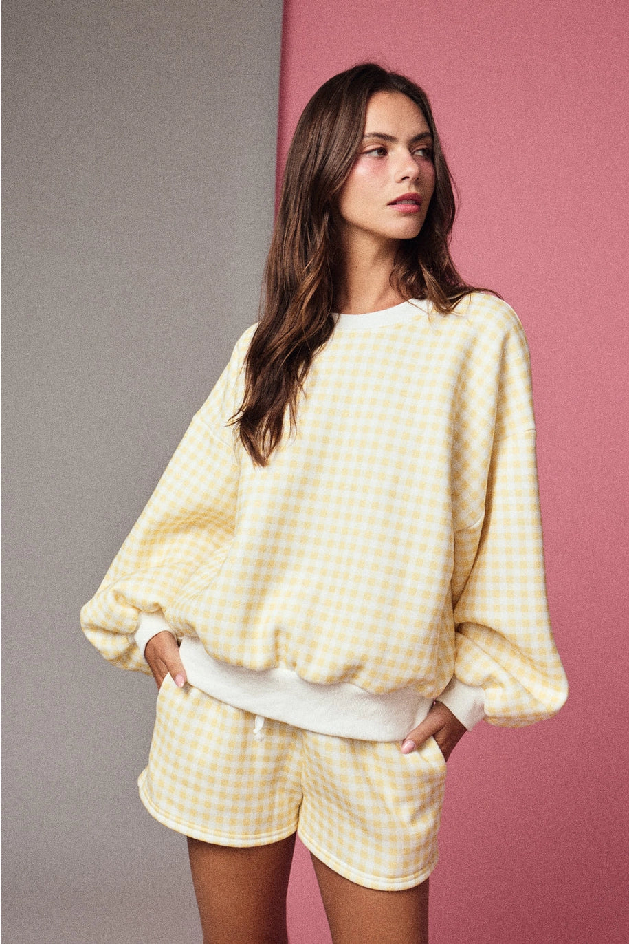 Woman wearing a yellow checkered outfit against a pink and gray background