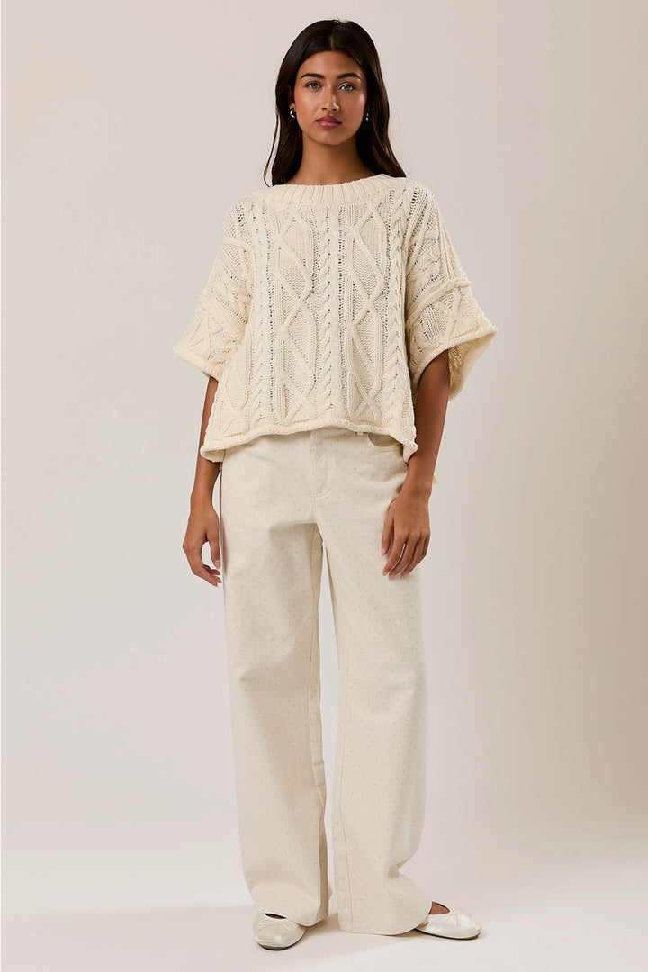 Woman wearing a cream-colored cable knit top and pants on a plain background