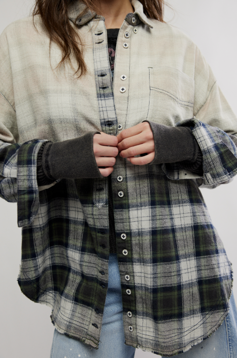 A person wearing a layered button-front shirt with a cream and gray plaid outer layer and dark charcoal fingerless sleeves, paired with light blue jeans against a plain light background.