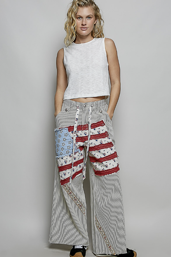 Woman wearing a white sleeveless top and patterned pants on a plain background