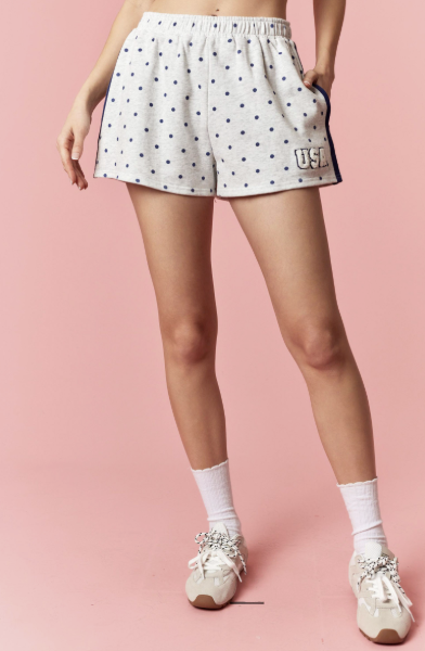 Person wearing grey shorts with navy polka dots on a pink background