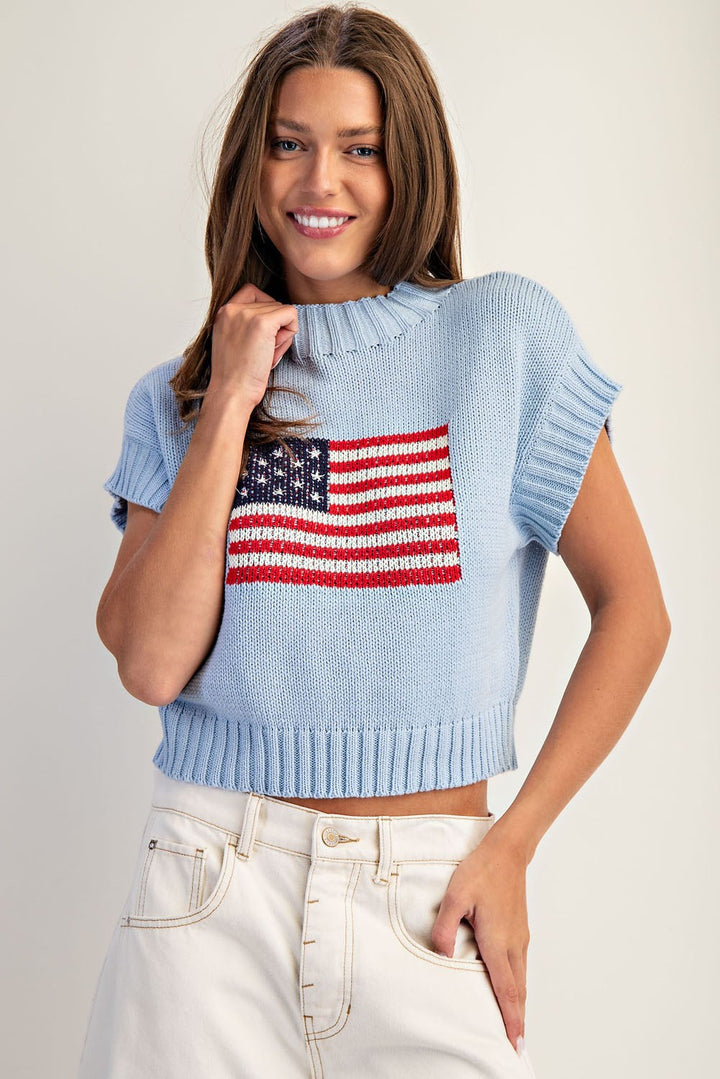 Woman wearing a light blue knit top with an American flag design on a plain background
