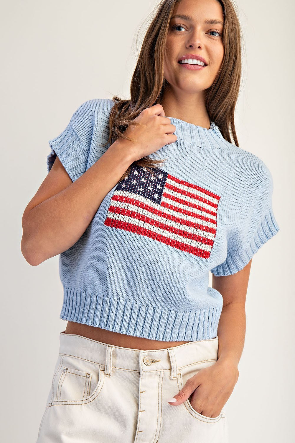 Woman wearing a light blue sweater with an American flag design on a plain background