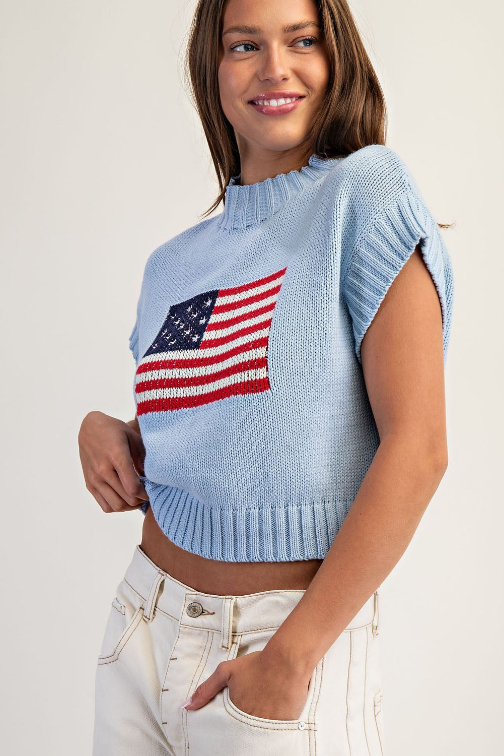Woman wearing a light blue sweater with an American flag design on a plain background
