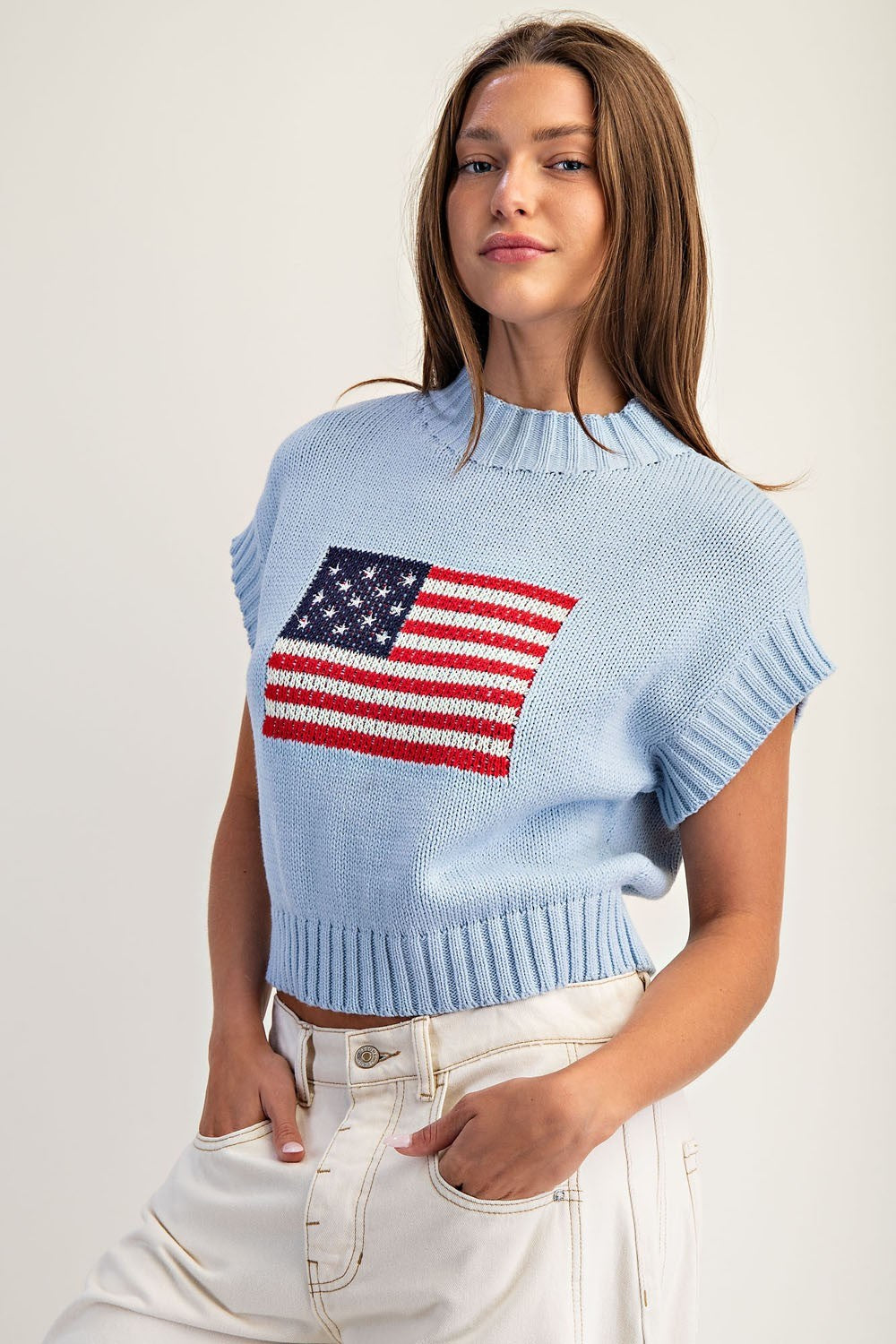 Woman wearing a light blue sweater with an American flag design on a plain background