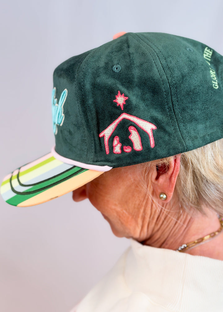 Woman wearing dark green suede trucker hat with manger embroidered on side on plain background