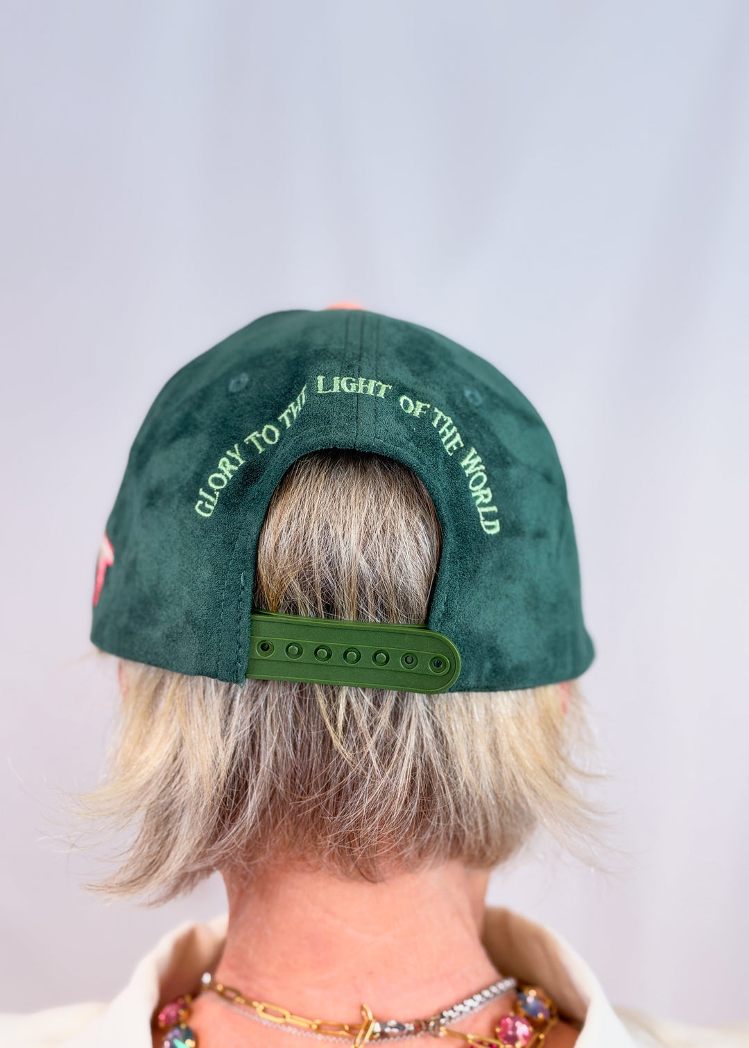 Woman shown from back wearing dark green suede trucker hat with &