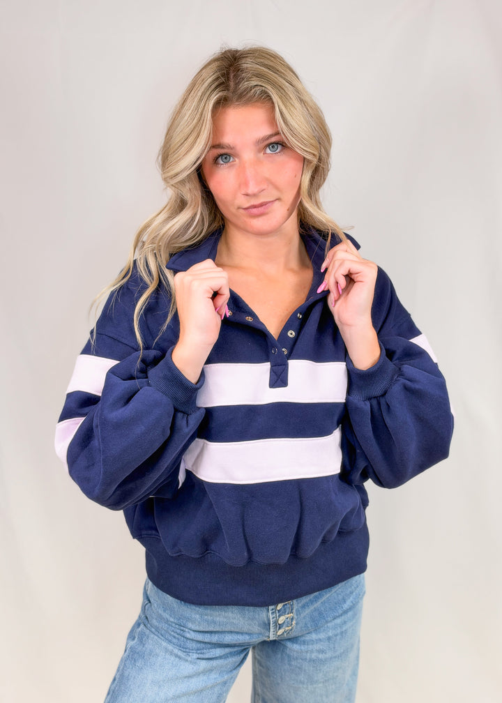 Woman wearing navy and lilac stripe snap collar pullover with jeans on plain background