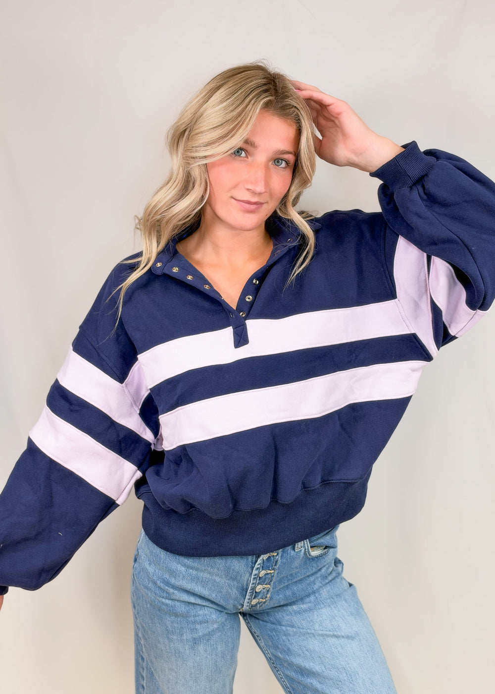 Woman wearing navy sweatshirt with lilac stripes and snap collar with jeans on plain background