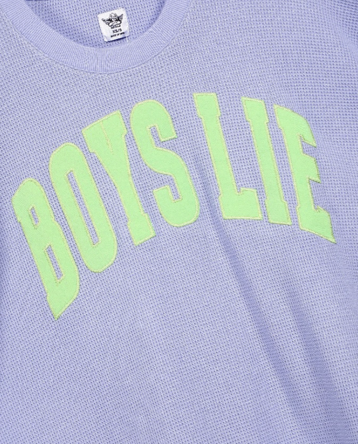 A close-up of a light lavender waffle-knit t-shirt featuring the phrase &