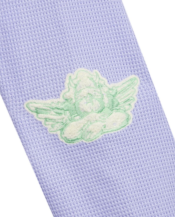 A close-up of a light lavender knit fabric with a mint green embroidered cherub motif on a white background.