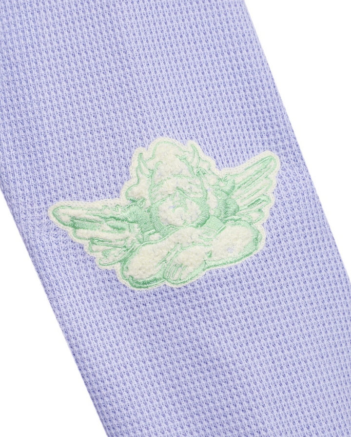 A close-up of a light lavender knit fabric with a mint green embroidered cherub motif on a white background.