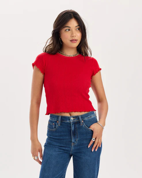 Woman wearing a red cropped top and blue jeans on a white background