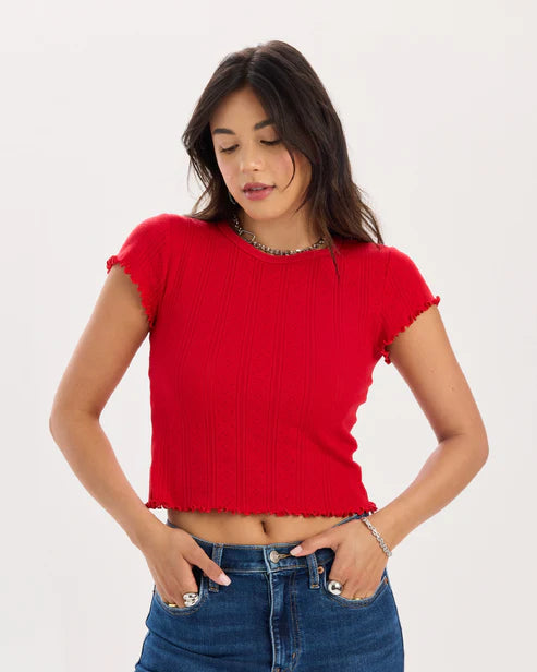 Woman wearing a red cropped top and blue jeans on a white background