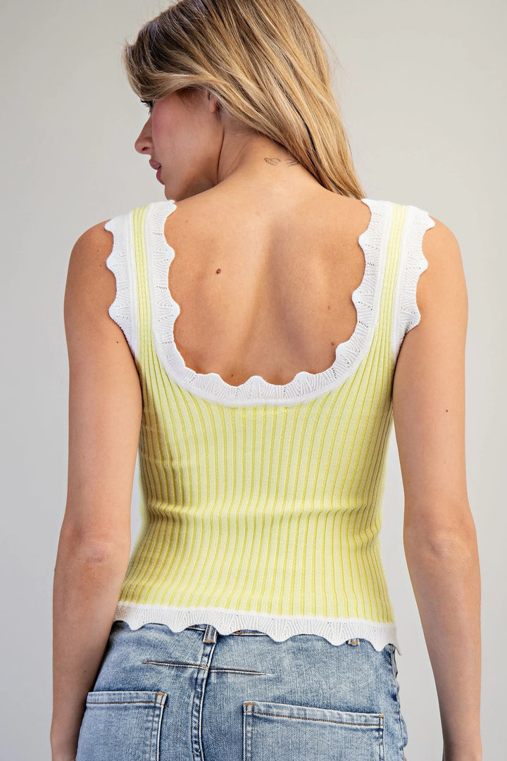 Woman wearing a light green tank top with white lace trim on a plain background