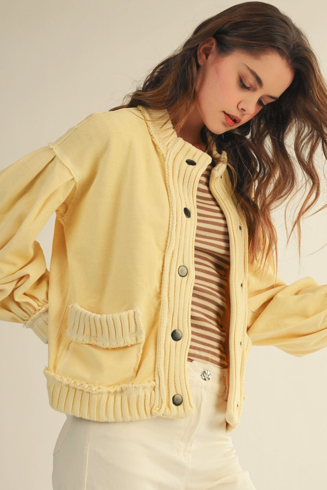 Woman wearing a yellow cardigan over a striped shirt on a plain background