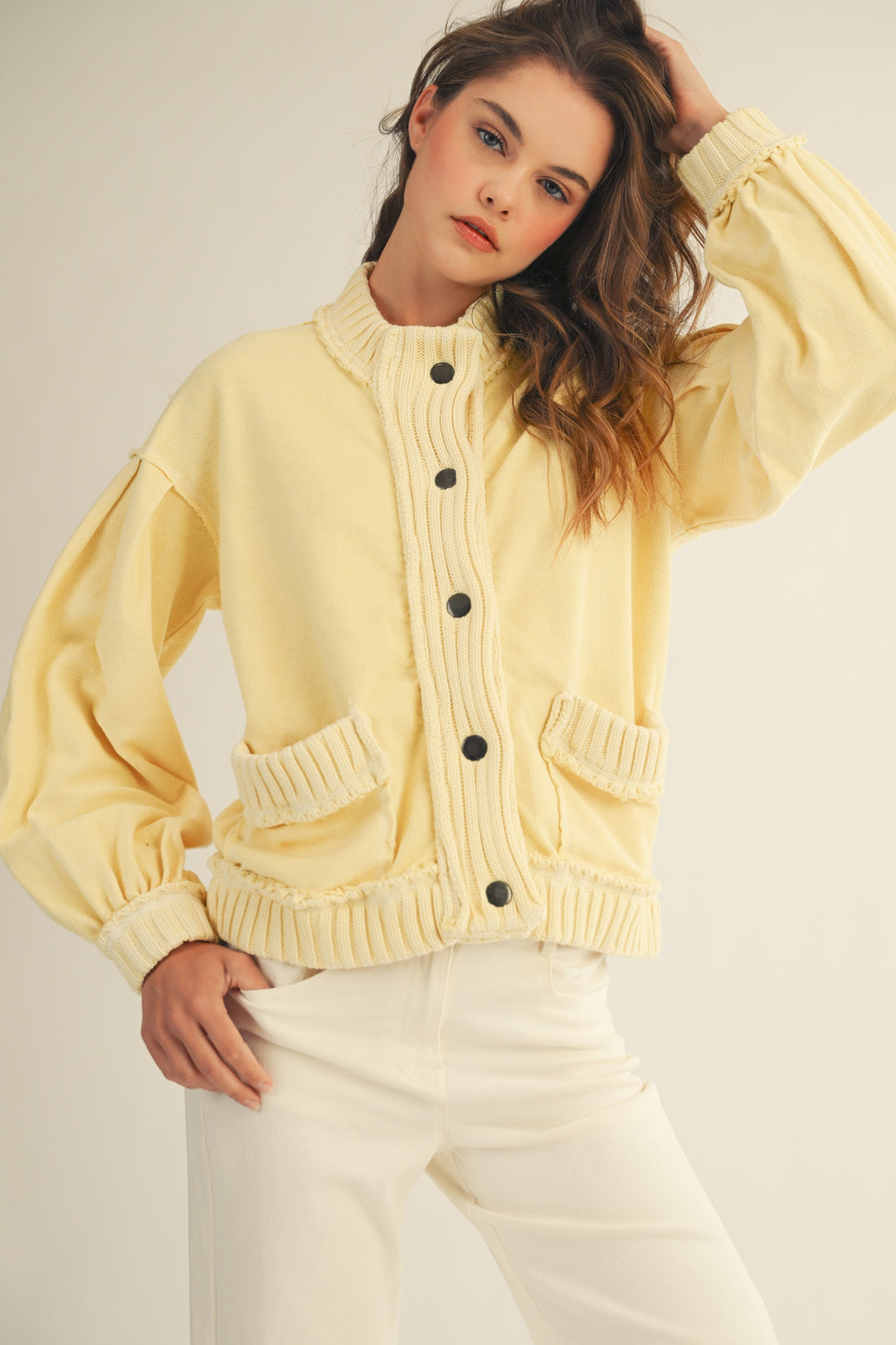 Woman wearing a light yellow cardigan with black buttons on a plain background