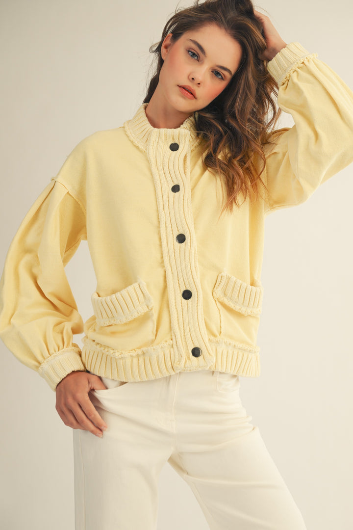 Woman wearing a light yellow cardigan with black buttons on a plain background
