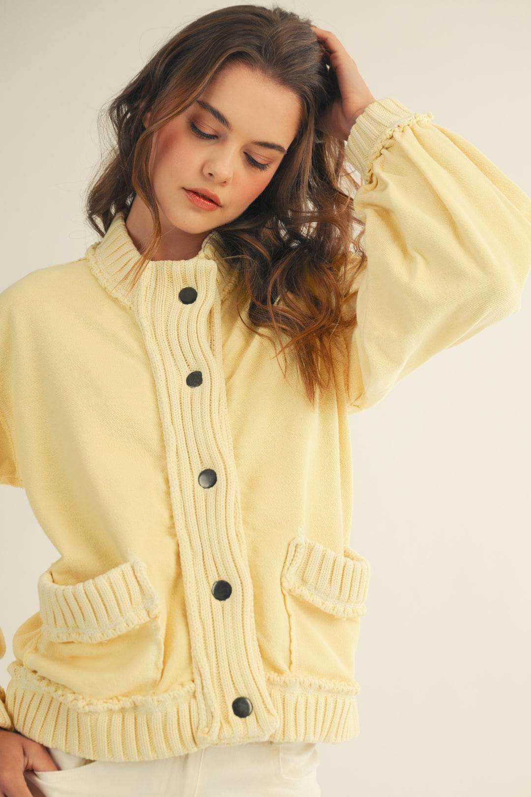 Woman wearing a light yellow cardigan with black buttons on a plain background