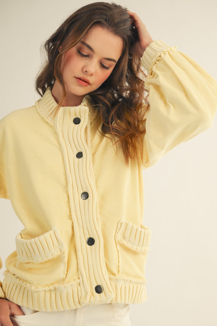 Woman wearing a light yellow cardigan with black buttons on a plain background