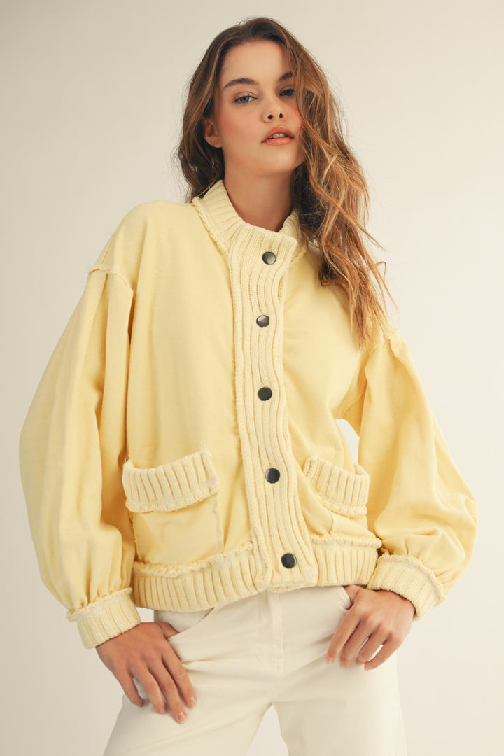 woman wearing yellow cardigan and white pants on plain background