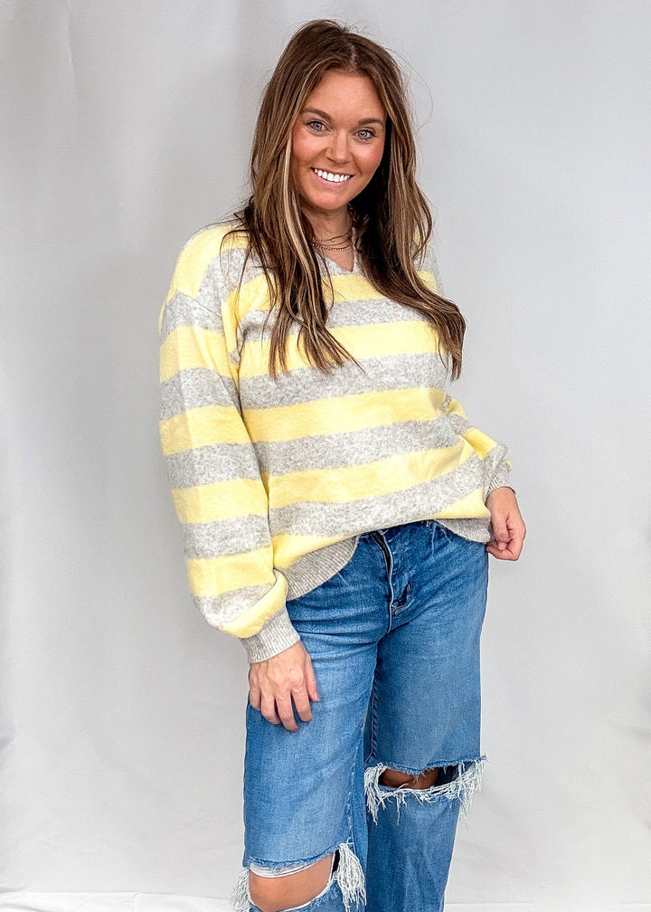 Woman wearing yellow and heather grey stripe sweater with jeans on plain background