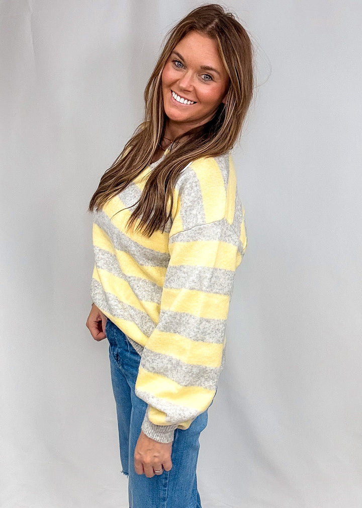 Woman wearing yellow and heather grey stripe sweater and jeans on plain background